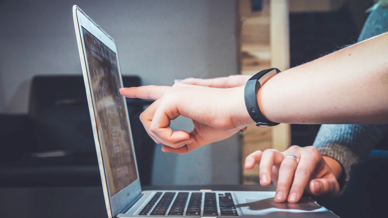 Two teammates point at a laptop while reviewing a creator profile