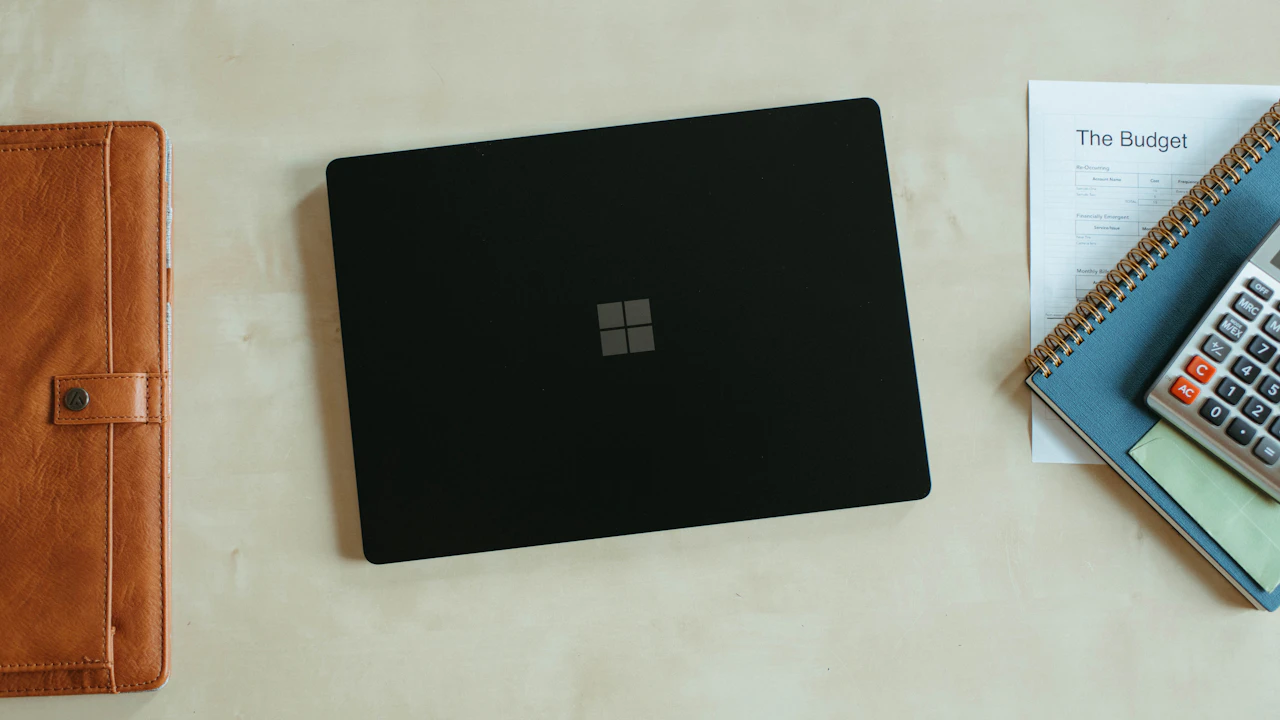 A laptop, calculator, notebook, and printed budget on a desk