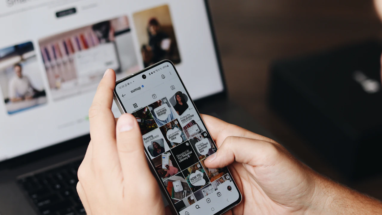 A person reviews social media content on a phone beside a laptop